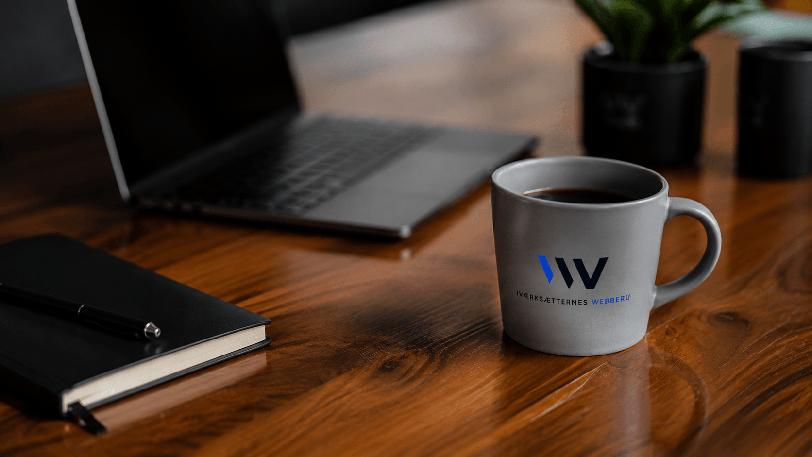 Kaffekop med Iværksætternes Webbureau-logo på skrivebord